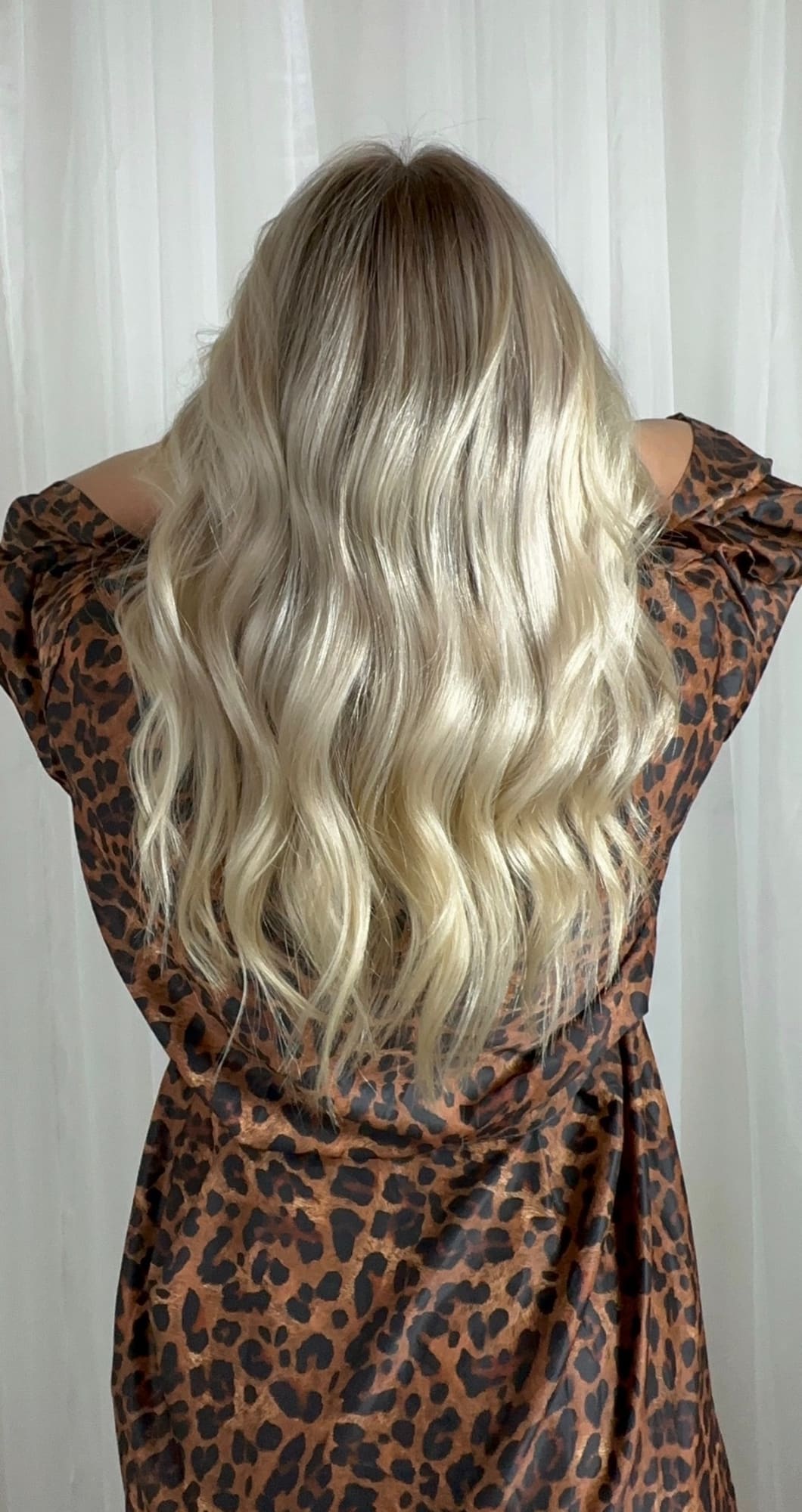 Woman with long blonde wavy hair wearing leopard print top, back view