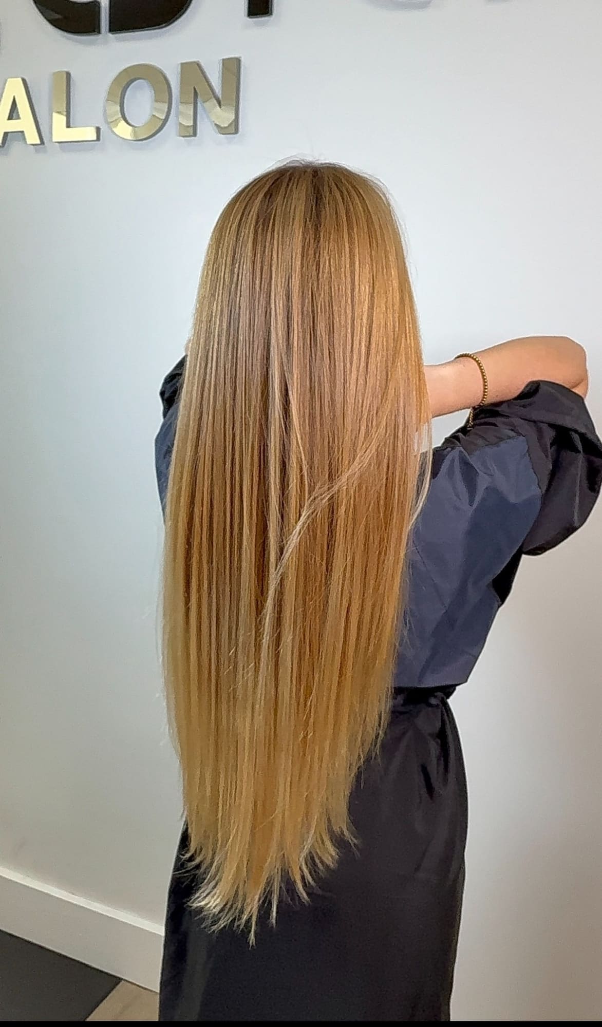 Woman with long golden blonde straight hair viewed from behind, wearing dark jacket