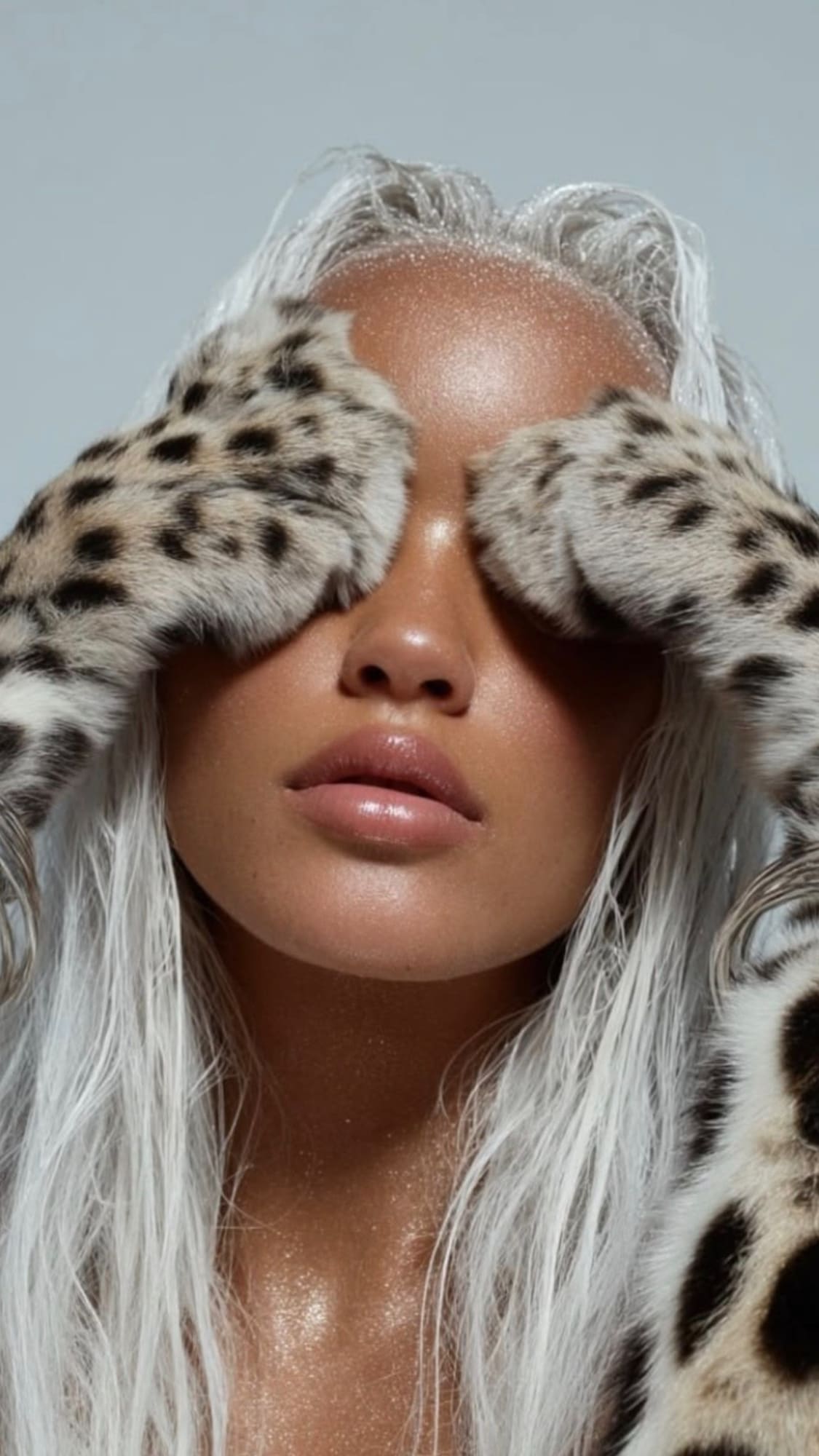 Person with silver hair and leopard print ear covers against gray background