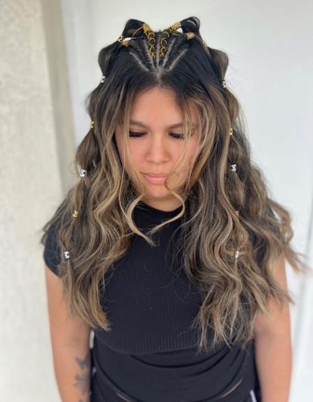 Woman with long wavy brunette hair, gold hair clips, and black choker looking downward