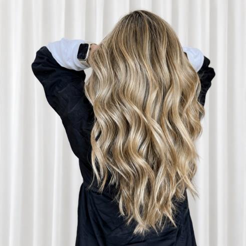 Woman with long blonde wavy hair viewed from behind against white curtains