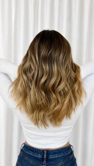 Woman with long wavy brunette hair with blonde highlights from behind