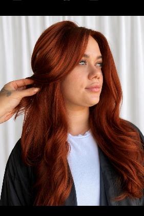 Woman with long wavy copper red hair wearing black cardigan over light blue top